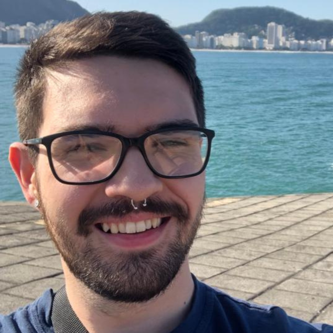 Foto do Pedro sorrindo com uma lagoa ao fundo